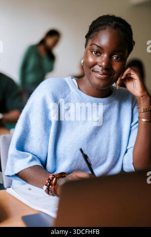 Smiling portrait of young woman sitting in classroom at college Stock Photo
