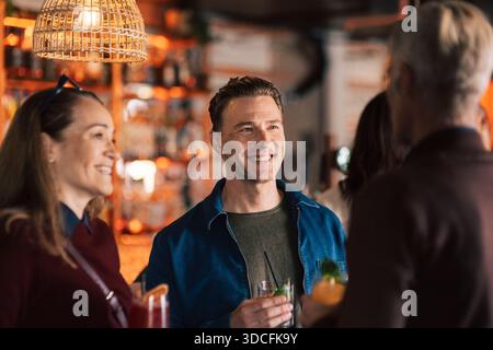 Smiling man holding drink and talking with friends in party at bar Stock Photo