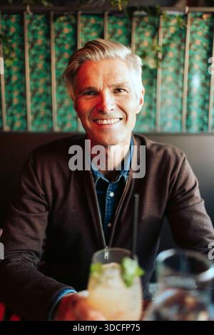 Portrait of smiling senior man sitting with drink at restaurant Stock Photo