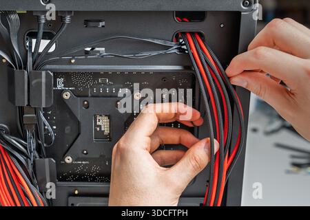 Close-up of hands installing red and black power cables inside a modern computer case. This careful work ensures proper connectivity for optimal performance, ideal for tech blogs or DIY guides. Stock Photo