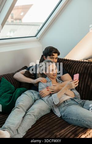 Young man sitting with girlfriend using smart phone while sitting on sofa in apartment Stock Photo