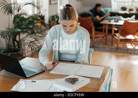Concentrated young woman doing bookkeeping while sitting at table in apartment Stock Photo