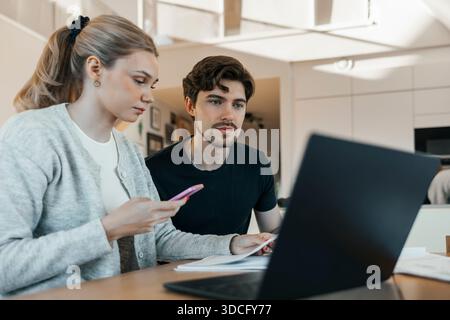Young man sitting with girlfriend using smart phone while calculating home budget Stock Photo