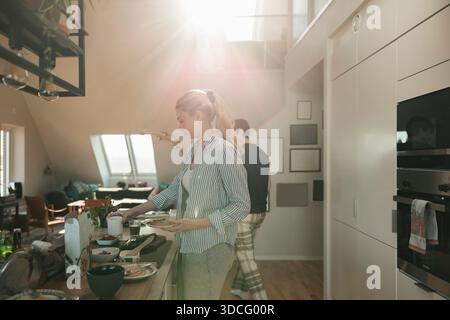 Young woman making breakfast in kitchen at home on sunny morning Stock Photo