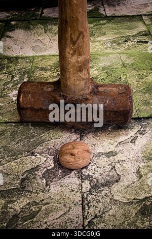Minimalist still life image of an old and worn sledge hammer and an unbroken nutshell relating to the saying "Using a sledge hammer to crack a nut" Stock Photo