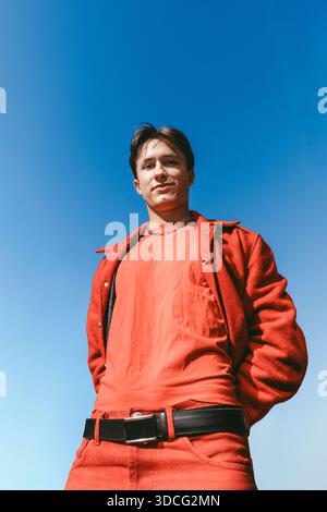 Low angle view of young man in red clothing posing under clear blue sky Stock Photo