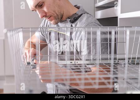 A man works on assembling a metal shelf inside a kitchen cabinet in daylight. Stock Photo