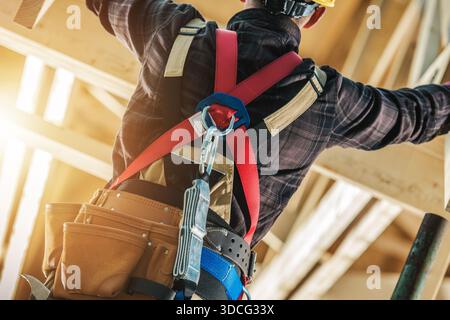 A worker in a safety harness uses tools while working on a construction site during the day. Stock Photo
