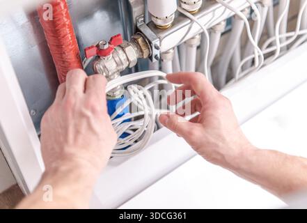 Hands are working on a plumbing system, adjusting a valve connected to various pipes. Stock Photo