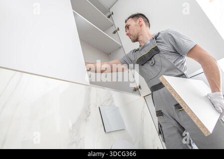 A worker organizes materials and installs shelves in new kitchen cabinets. The task is part of a home renovation effort. Stock Photo