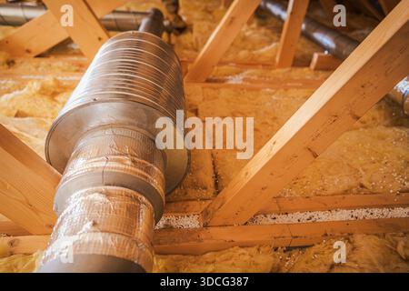 A view of duct work and pipes in an attic. Insulation is placed on the floor and wooden beams support the structure. Stock Photo