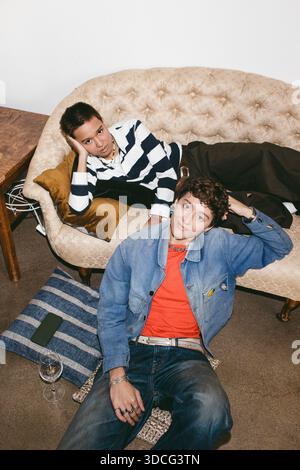 High angle portrait of young woman sitting near transgender friend lying on sofa Stock Photo
