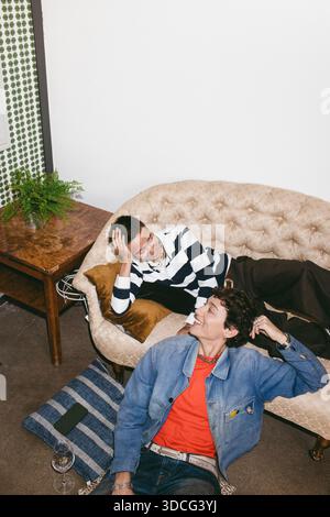 High angle view of smiling young woman talking with non-binary friend lying on sofa in home Stock Photo
