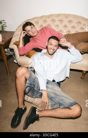 High angle portrait of smiling young man sitting near male friend lying on sofa Stock Photo