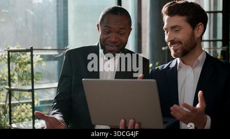 Two excited business team men businessmen looking laptop screen happy communicate in office discussing good idea excellent result project success Stock Photo