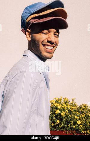 Smiling man winking while wearing multi colored caps against wall Stock Photo