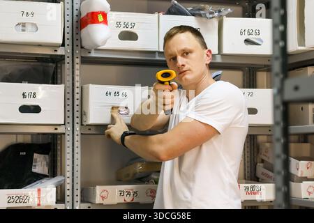 Male employee uses barcode scanner on package among shelves in storage area Stock Photo