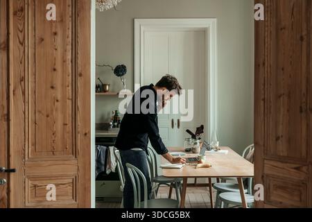 Businessman talking on phone while writing in diary at home Stock Photo