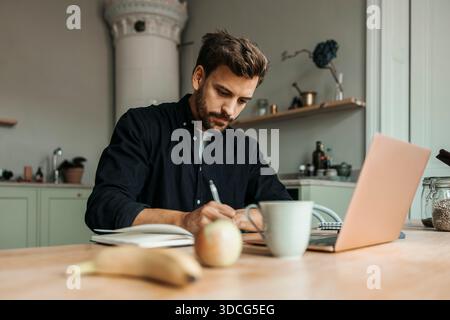 Focused male freelancer writing in diary while working from home Stock Photo