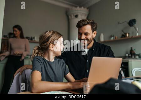 Smiling man talking with daughter using laptop at home Stock Photo