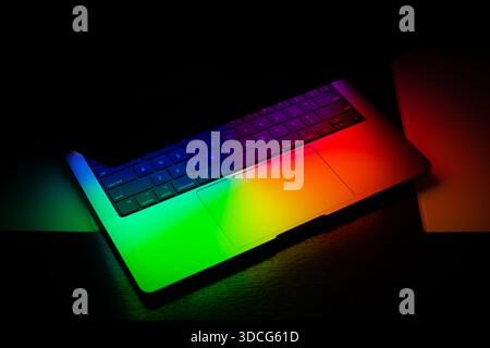 Laptop Screen Glowing in Purple Yellow Blue Neon Light in Black Background Stock Photo