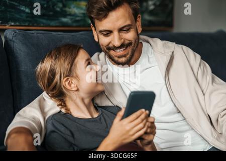 Happy girl using smart phone while sitting with father at home Stock Photo