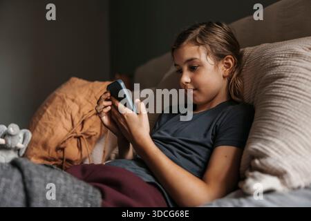 Girl using smart phone while lying on bed in home Stock Photo