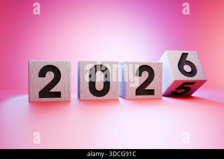 Wooden cubes with numbers forming 2026, symbolizing the upcoming new year, transition from 2025 to 2026, on a pink blue gradient, concept of future an Stock Photo