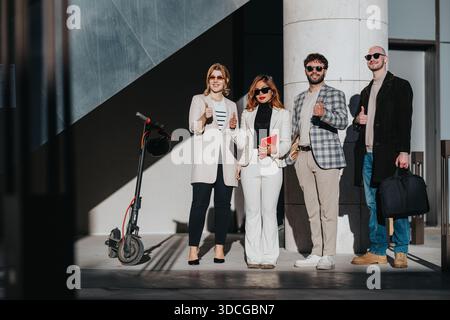 Group of four business professionals posing outside a modern building with thumbs up for teamwork Stock Photo