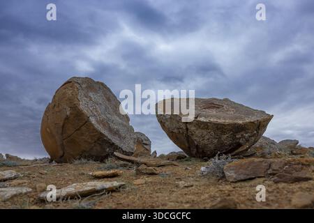View of split, spherical rock formations scattered across the arid landscape under a dramatic sky, Shetpe, Mangystau Region, Kazakhstan. Stock Photo