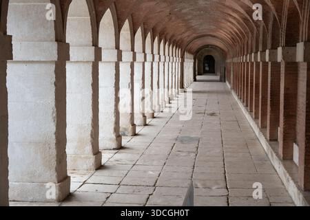 A long corridor with arches and columns, featuring a stone floor and brick walls, creating a serene architectural space Stock Photo
