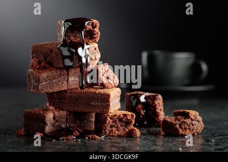 Brownie pieces on a black background. Melted chocolate drips down the brownie. Copy space. Stock Photo