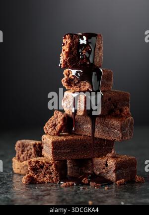 Brownie pieces on a black background. Melted chocolate drips down the brownie. Stock Photo