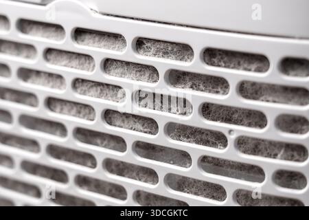 Clogged intake filter in household air purifier with thick layers of accumulated dust and fibers on a plastic ventilation grille Stock Photo