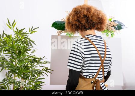 Artist with curly hair stands in front of a blank canvas on an easel, ready to paint Stock Photo