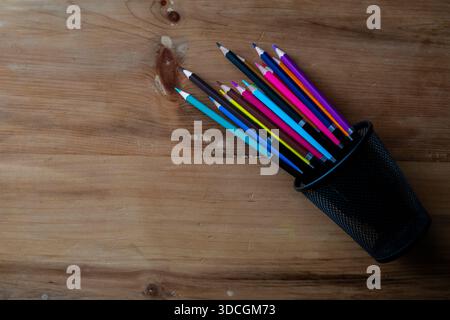 Top view of colored pencils in fallen pen holder on wooden desk. Stock Photo