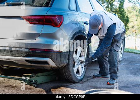 Hands-on independence shown through a senior man changing a car tire, carefully loosening wheel bolts and relying on experience, focus, and practical Stock Photo