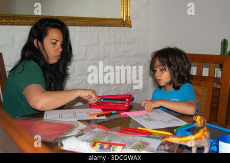 Mother assisting her son with homeschooling, using colored pencils and paper on the dining table Stock Photo