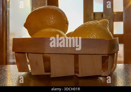 Fresh yellow lemons in wooden basket on dark rustic wooden table Stock Photo