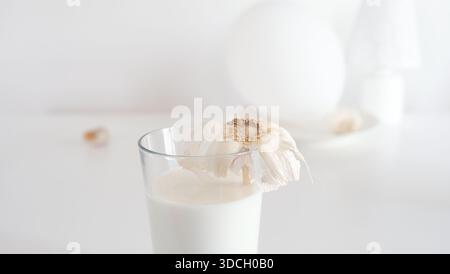 A minimalist still life featuring a glass of milk with garlic in a soft white interior setting. The image is suitable for modern food styling, neutral Stock Photo
