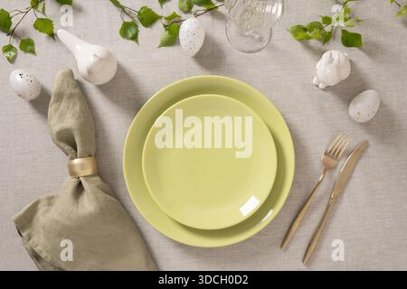 Elegant Easter place setting with pastel green plates, linen napkin, golden cutlery and spring decor on neutral textile background, flat lay composition. Stock Photo