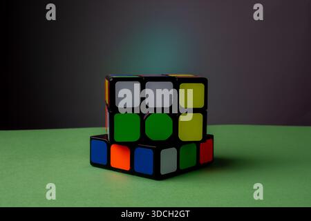 Partially solved Rubik's Cube on a green surface with a dark background. Stock Photo
