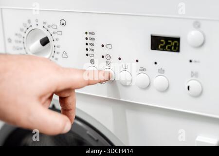 Close-up of a hand interacting with a washing machine control panel, featuring buttons and a digital display, highlighting the functionality of laundr Stock Photo