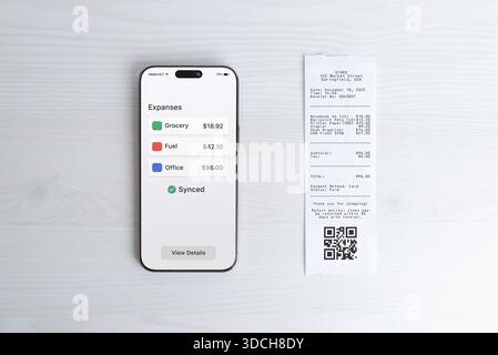 Smartphone displaying expense overview dashboard next to paper receipt, modern bookkeeping and finance app concept for business reporting, analytics, Stock Photo