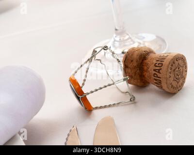 CHAMPAGNE CORK FINE DINING Veuve Clicquot Luxury dining table setting with  vintage rosé champagne cork and wire cage muselet on tablecloth with napkin and place setting Stock Photo