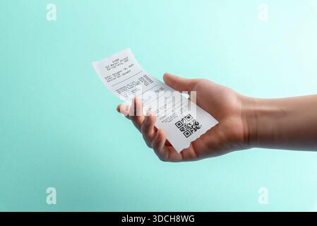 Hand holding paper receipt with qr code on blue background, digital payment and expense tracking concept for fintech apps, accounting software, and re Stock Photo