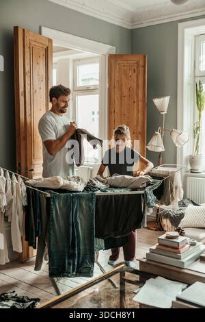 Father and daughter folding clothes on drying rack in home Stock Photo