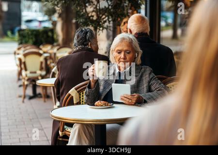 Senior woman having coffee while using tablet PC at sidewalk cafe Stock Photo