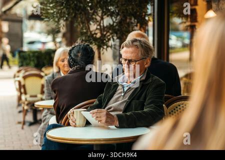 Senior man using digital tablet while sitting at sidewalk cafe Stock Photo