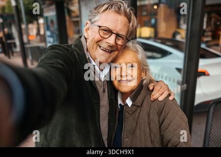 Portrait of smiling senior man taking selfie with woman at bus stop Stock Photo